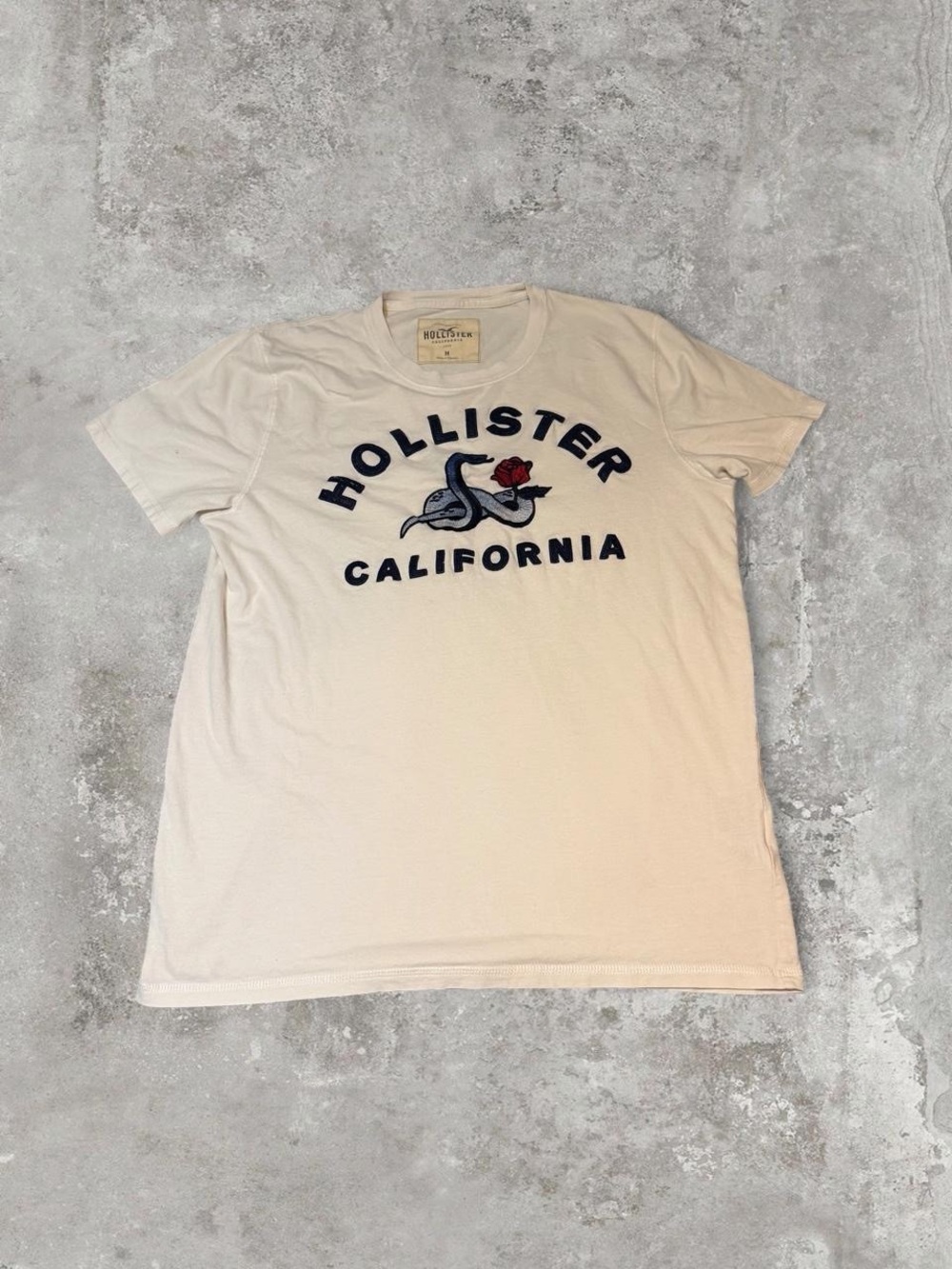 Hollister Men’s Cream Short-Sleeve Tee with Navy Logo and Red Rose Accent Size M
